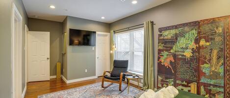 Quarto com cama verde, uma cadeira de balanço, tapete estampado, televisão e um painel decorativo.