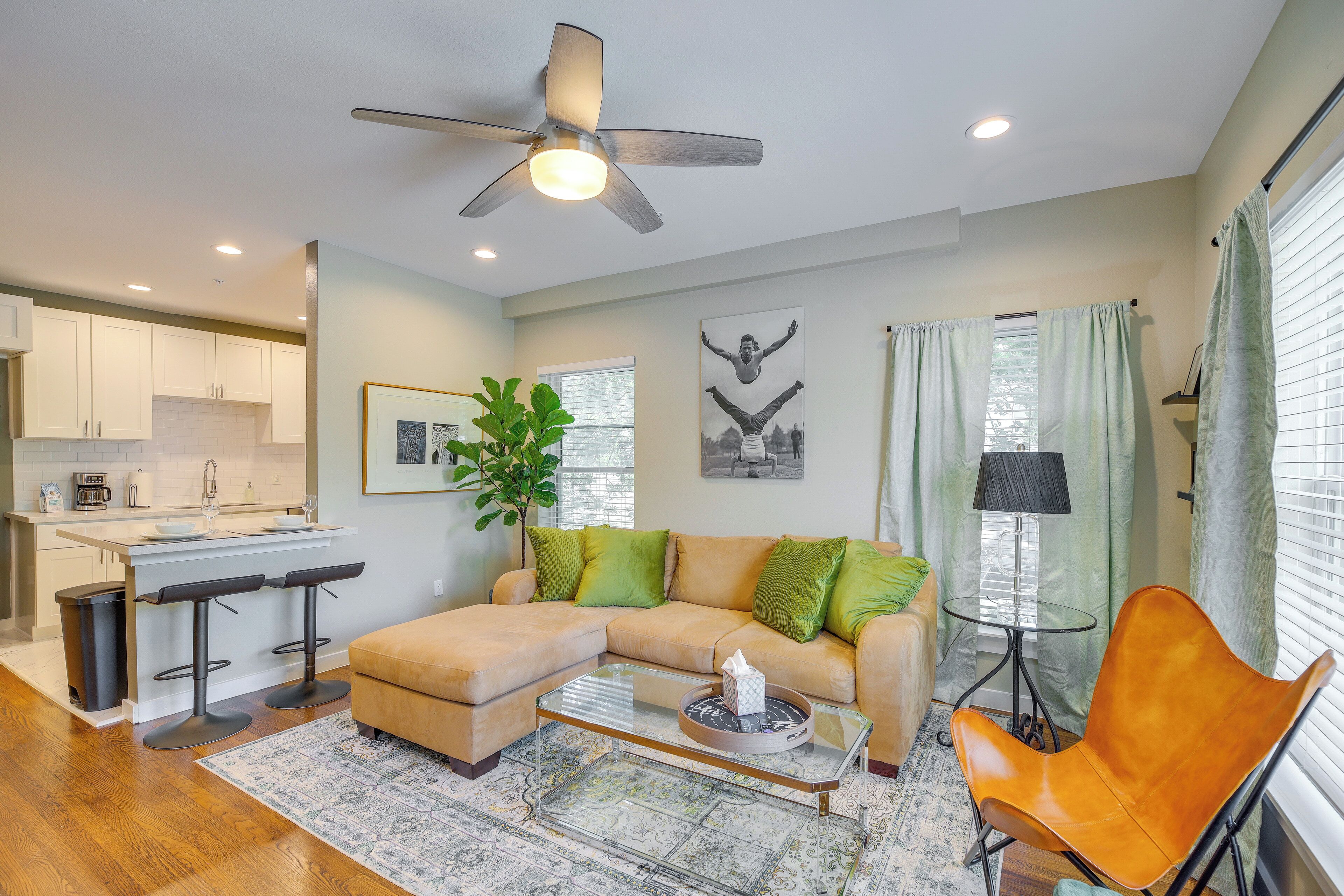A modern living room with a sectional sofa, a glass coffee table, a bar stool, and a ceiling fan.