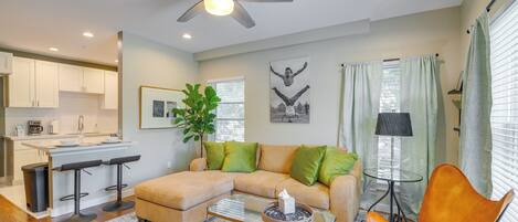 A modern living room with a sectional sofa, a glass coffee table, a bar stool, and a ceiling fan.