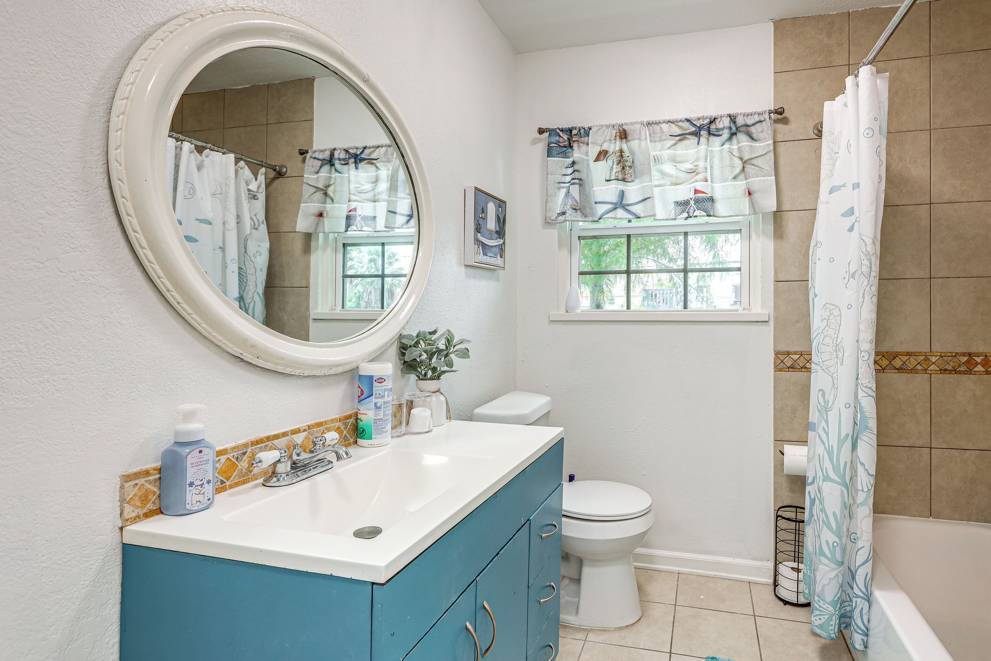 Une salle de bain avec un lavabo blanc, un meuble-lavabo bleu, des toilettes blanches et un rideau de douche à motifs marins.