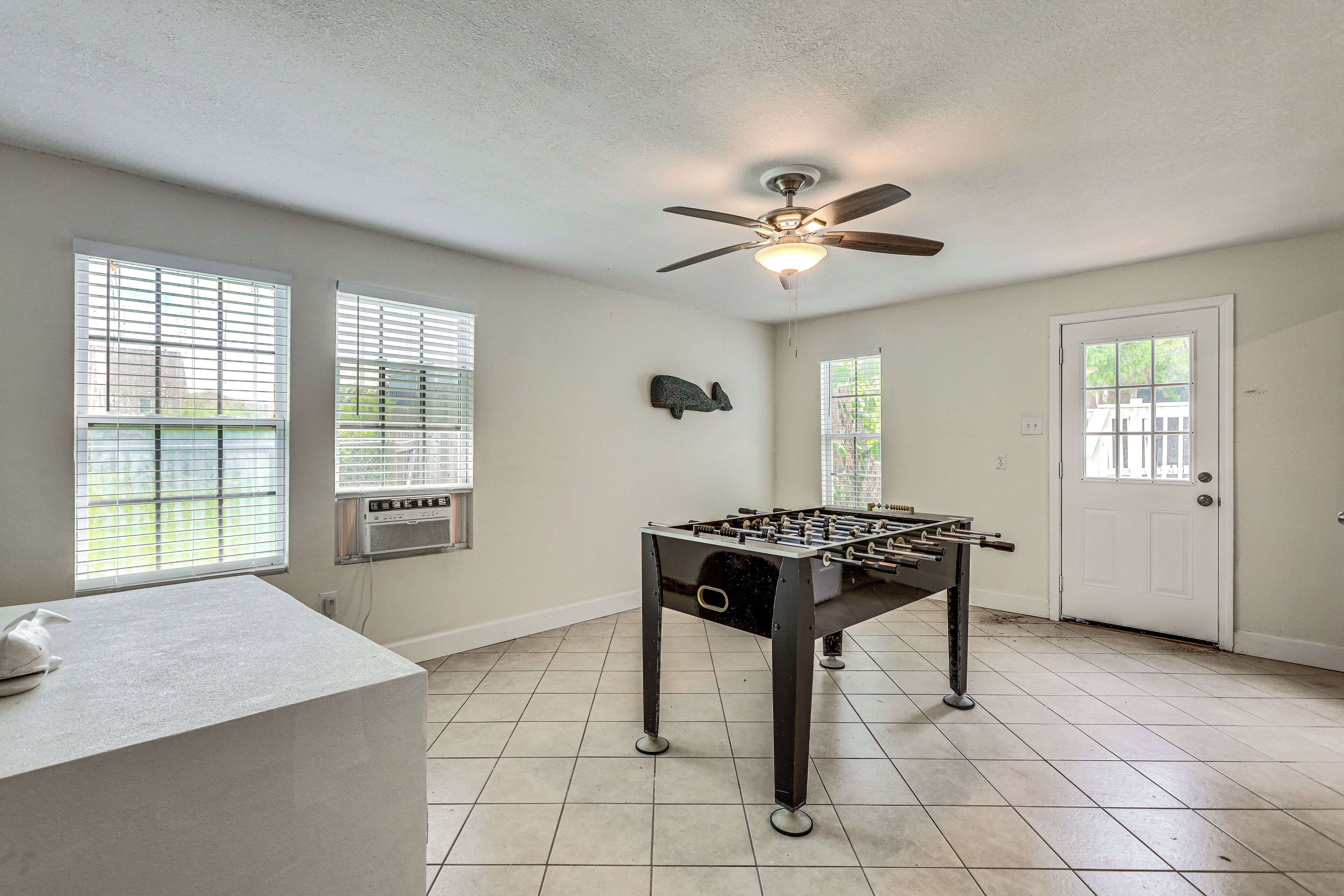 A room with a foosball table, a ceiling fan, and a door with a window.