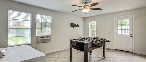 A room with a foosball table, a ceiling fan, and a door with a window.