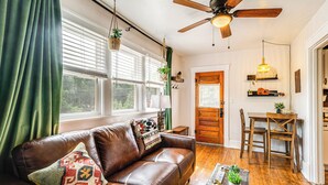 A cozy living room with a brown leather sofa, a wooden dining table, and a ceiling fan. - Manitou Mountain Retreat: Deck & Fire Pit! (Manitou Springs)