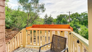 A balcony with a wooden railing, a chair, and a view of trees and a road. - Manitou Mountain Retreat: Deck & Fire Pit! (Manitou Springs)