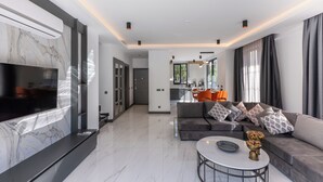 A modern living room with a large flat-screen TV, a marble accent wall, a grey sofa with patterned cushions, and a round coffee table. - Minta Hills Villas Kemer (Kemer)