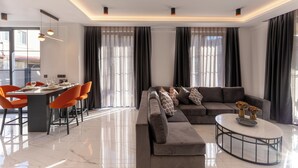 A modern living room with a dining area, featuring a sectional sofa, orange chairs, a round coffee table, and a glass-top dining table. - Minta Hills Villas Kemer (Kemer)