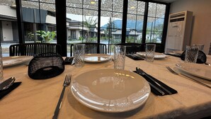 A dining table set with plates, cutlery, and glasses, with a view of a building and mountains through large windows. - Minta Hills Villas Kemer (Kemer)