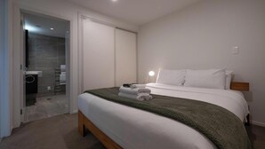 Une chambre d’hôtel avec un lit, une lampe de chevet et une salle de bain visible à travers une porte en verre.