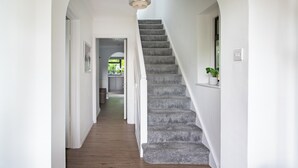 Un escalier recouvert d’une moquette grise menant à un palier, des murs blancs et un luminaire au plafond.