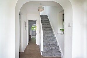 Un escalier recouvert d’une moquette grise menant à un palier, des murs blancs et un luminaire au plafond.