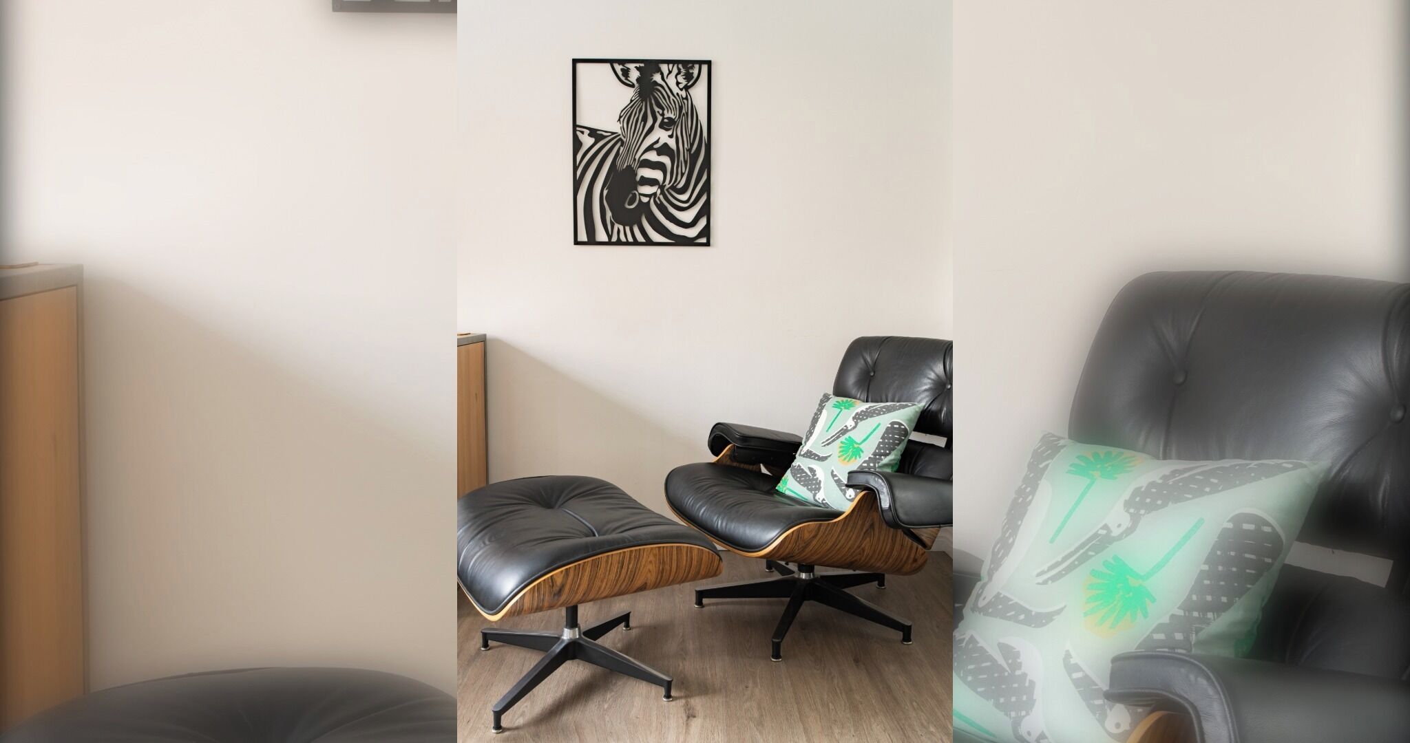 Een kamer met een zwarte leren fauteuil, een houten bijzettafeltje en een wanddecoratie met een zebra thema.