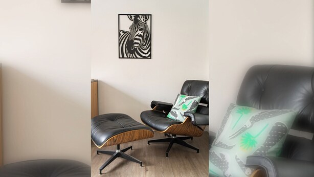 Une pièce comprenant un fauteuil en cuir noir, une table d’appoint en bois et une œuvre d’art sur le thème des zèbres accrochée au mur.