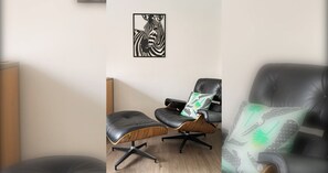 A room with a black leather chair, a wooden side table, and a zebra-themed artwork on the wall.