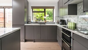 Une cuisine moderne avec des meubles gris, un plan de travail en marbre, une fenêtre donnant sur un espace verdoyant et un four encastré.