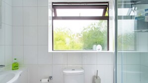 A bathroom with a toilet, bidet, and a window with a view of greenery. - Charming Retreat Near Grange Hill (Central Line) (Greater London)