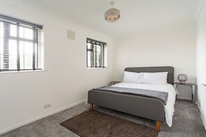 A bedroom with a bed, a nightstand, a lamp, a window, and a ceiling light.