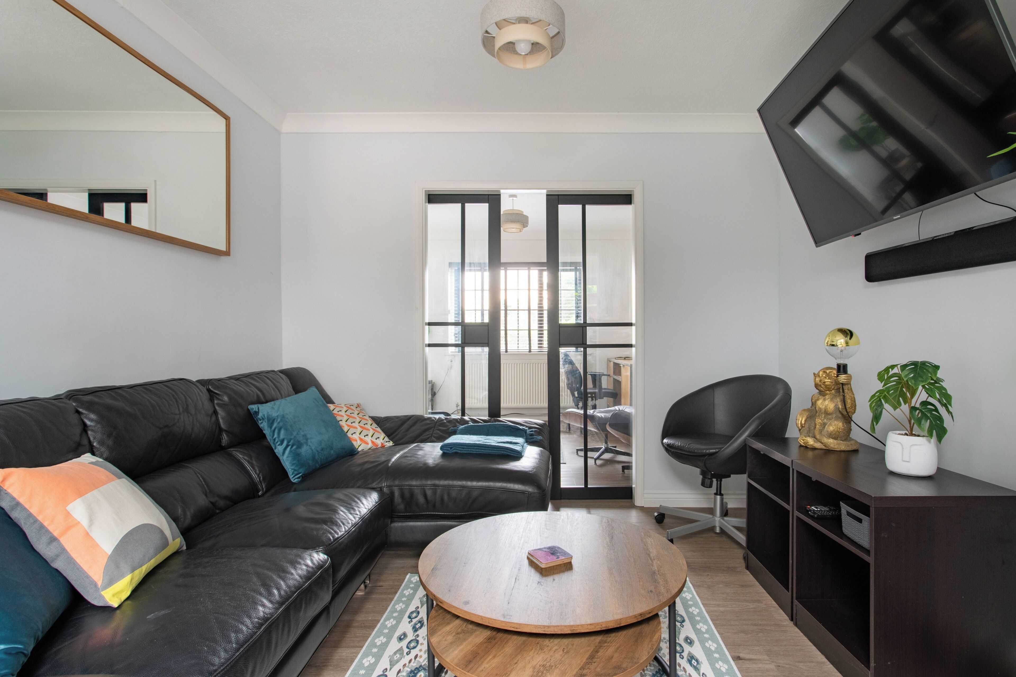 A modern living room with a black leather sofa, a round wooden coffee table, and a flat-screen TV mounted on the wall.