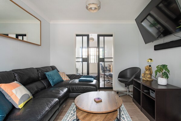 A modern living room with a black leather sofa, a round wooden coffee table, and a flat-screen TV mounted on the wall.