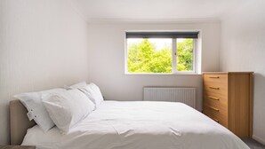 A bedroom with a bed, a window with a view of trees, a radiator, and a wooden dresser. - Charming Retreat Near Grange Hill (Central Line) (Greater London)