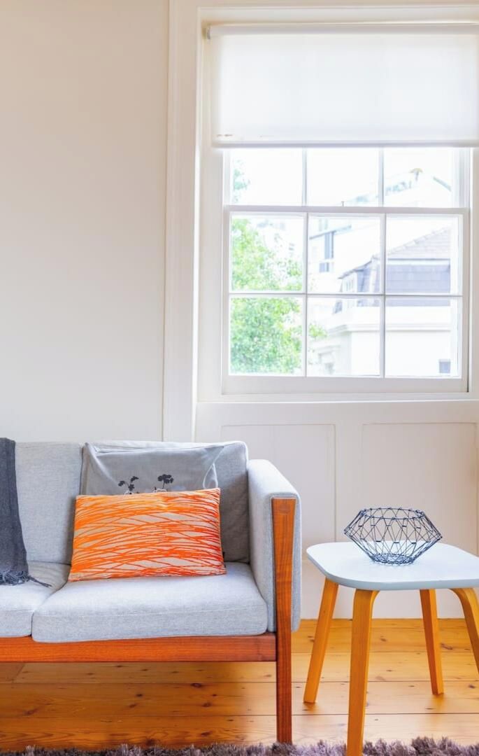 A room with a sofa, a small table, and a window with a view of buildings.