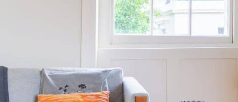 A room with a sofa, a small table, and a window with a view of buildings.