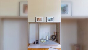 Habitació amb sòl de fusta, una estant amb quadres emmarcados i una taula petita amb espelmes i un vas.