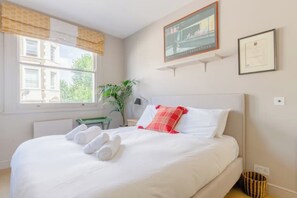 Et hotelværelse med en seng, et vindue med gardiner, en plante og et indrammet certifikat på væggen.