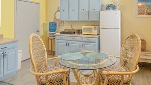 A compact kitchen with a round glass table, wicker chairs, and light blue cabinets.