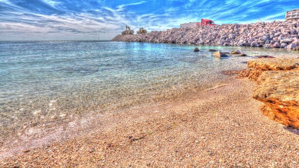 A beach with clear water, pebbles, and a rocky shoreline.