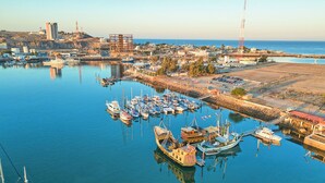 A marina with various boats docked, a waterfront promenade, and buildings in the background.