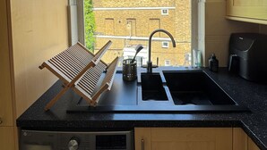 A compact kitchen with a washing machine, a sink, and a window overlooking a brick building. - Hidden Gem w/Private Terrace, Fulham Broadway! (London)