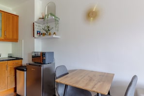 Et kompakt køkken med køleskab, mikroovn og et lille spisebord med stole.