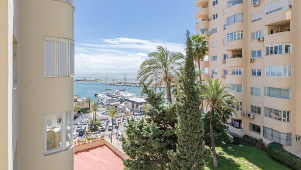 A high-rise building with balconies overlooking a marina and the sea.