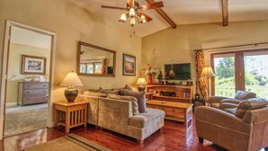 Un amplio salón con ventilador de techo, muebles de madera, chimenea y un gran ventanal con cortinas.