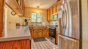 Una cocina con armarios de madera, un refrigerador de acero inoxidable, una estufa y un ventanal con vistas a la vegetación.