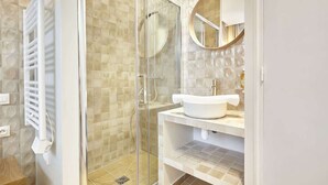 Une salle de bain moderne avec une douche à parois de verre, un lavabo blanc et un miroir rond.