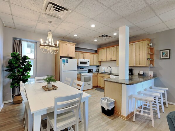 A modern kitchen with wooden cabinets, a central island, and a dining area with white furniture.