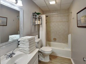 A bathroom with a sink, toilet, and bathtub. There is a towel rack with folded towels, a mirror, and a framed picture on the wall.