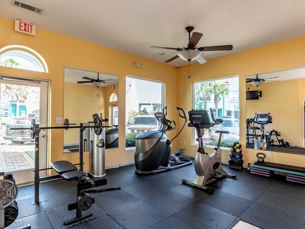 Ein Fitnessraum mit Trainingsgeräten, Deckenventilator und großen Fenstern.