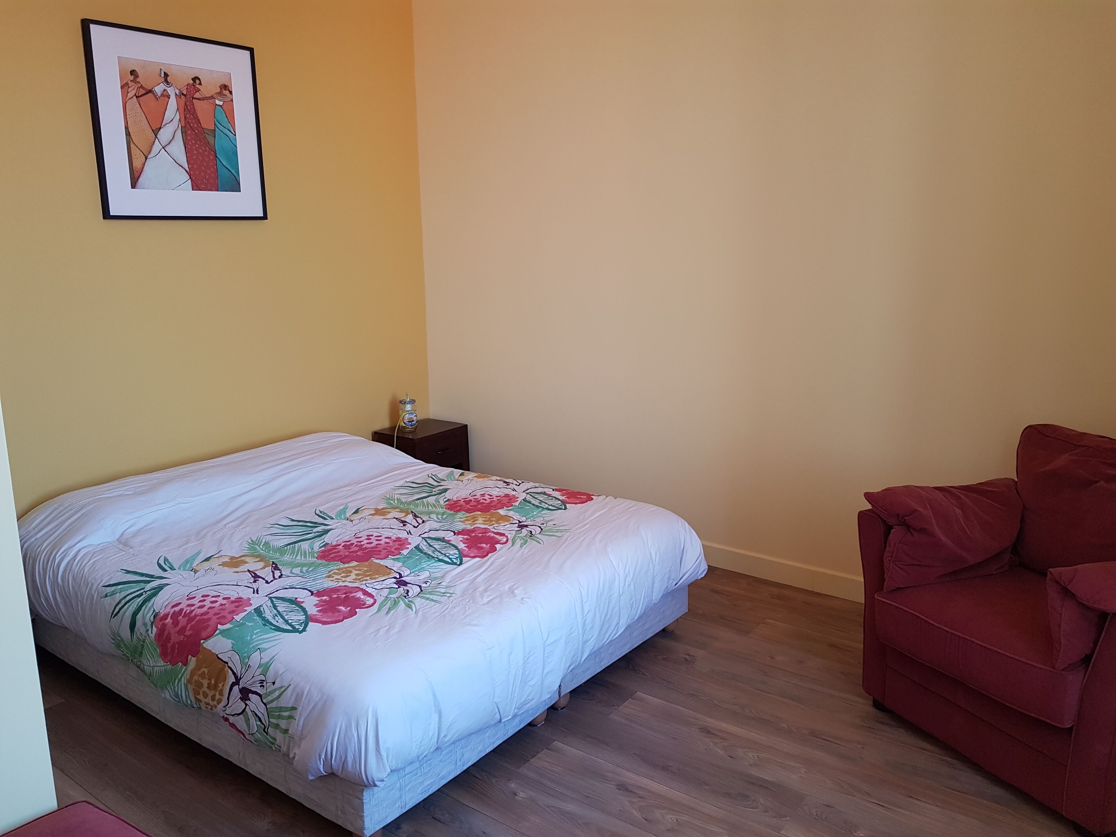 A bedroom with a bed, a nightstand, a red chair, and a framed picture on the wall.