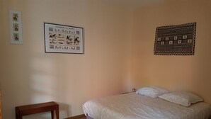 Un dormitorio con una cama, un banco de madera, un calendario en la pared y un tapiz estampado.