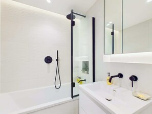 Ein modernes Badezimmer mit einer gläsernen Dusche, einem weißen Waschbecken mit zwei Wasserhähnen und einem Spiegel darüber.