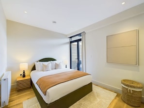 Une chambre à coucher avec un lit, une table de chevet, une lampe et une vue sur l’extérieur.