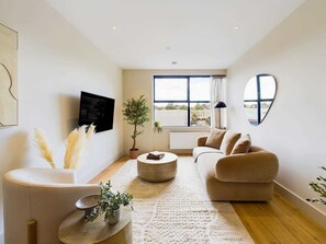 A modern living room with a sofa, a coffee table, a TV, a potted plant, and a large window. - Modern Apartment with Balcony near King's Cross (Greater London)