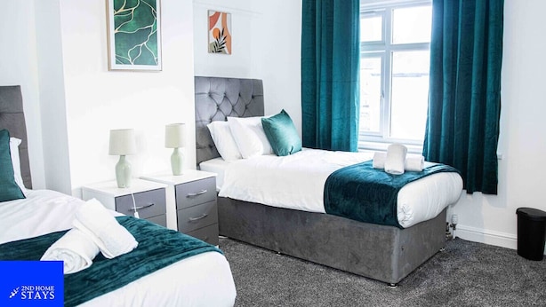 A hotel room with two beds, a grey headboard, teal curtains, and artwork on the walls.