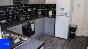 A compact kitchen with black and white tiles, a stove, oven, microwave, and a white refrigerator.