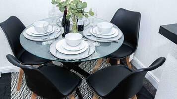 A round glass table with white plates, black chairs, and a vase with green leaves.