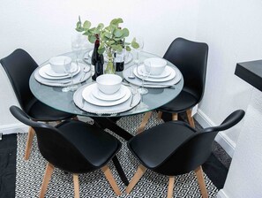 Ein runder Glastisch mit weißen Tellern, schwarzen Stühlen und einer Vase mit grünen Blättern.
