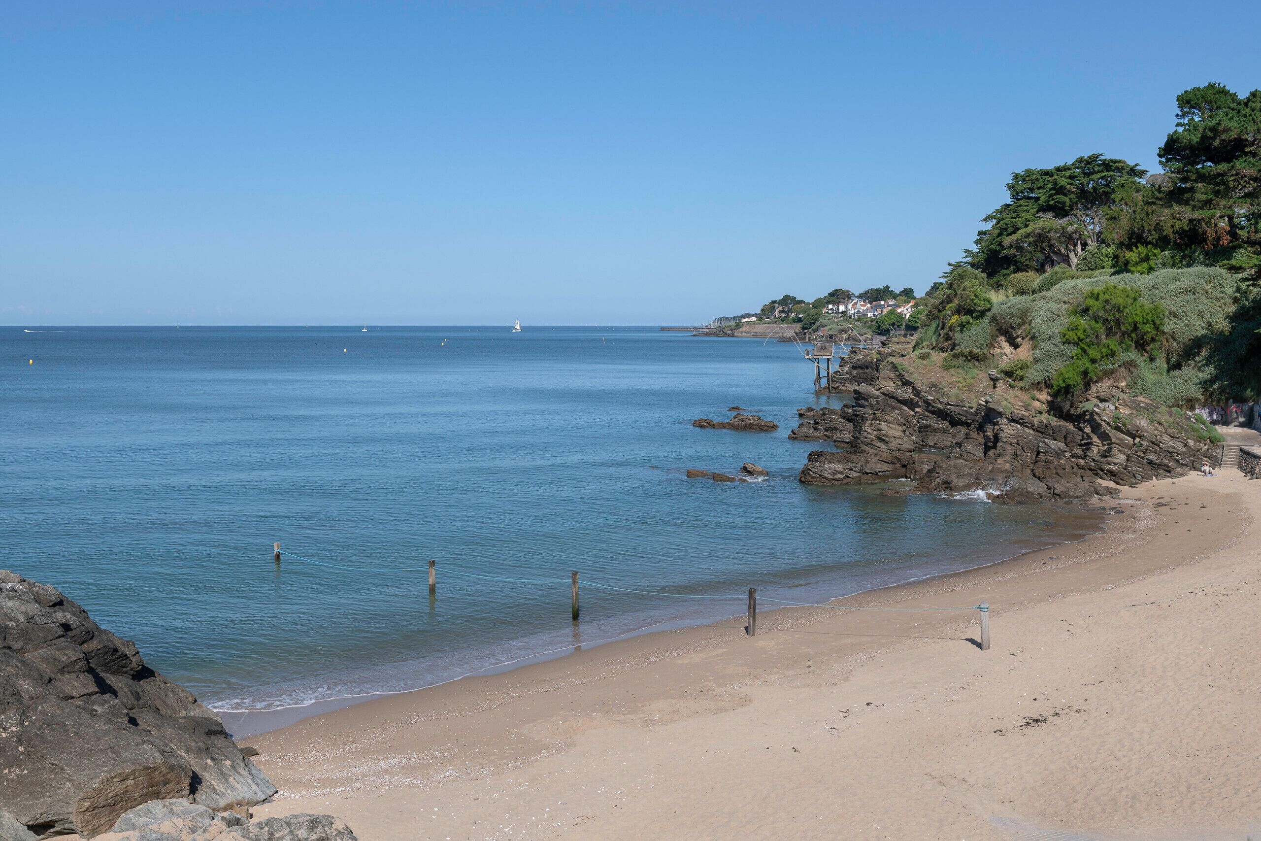 A beach with clear blue water, rocky outcrops, and a few people in the distance.