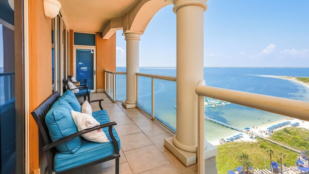 A balcony with a view of the ocean, a seating area with blue cushions, and a railing. - Last Minute Rates! P4-1202 - 2B Portofino Island Views! (Pensacola Beach)